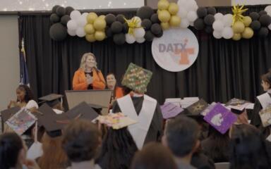photo from the DATX graduation. Behind students with an administrator at the podium speaking