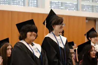 Students in caps and gowns smile during a graduation ceremony.