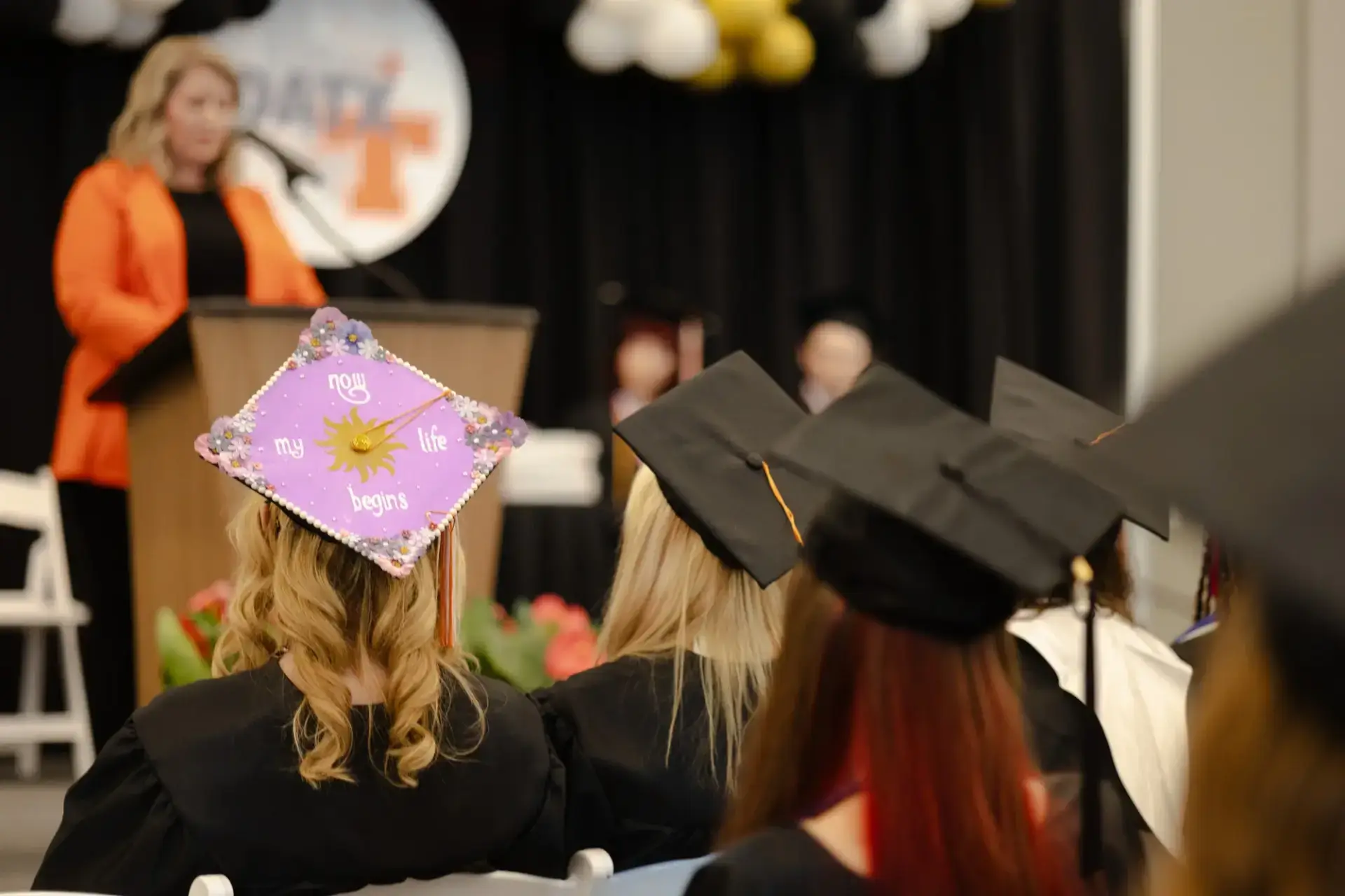Graduates in caps and gowns are seated at a ceremony.