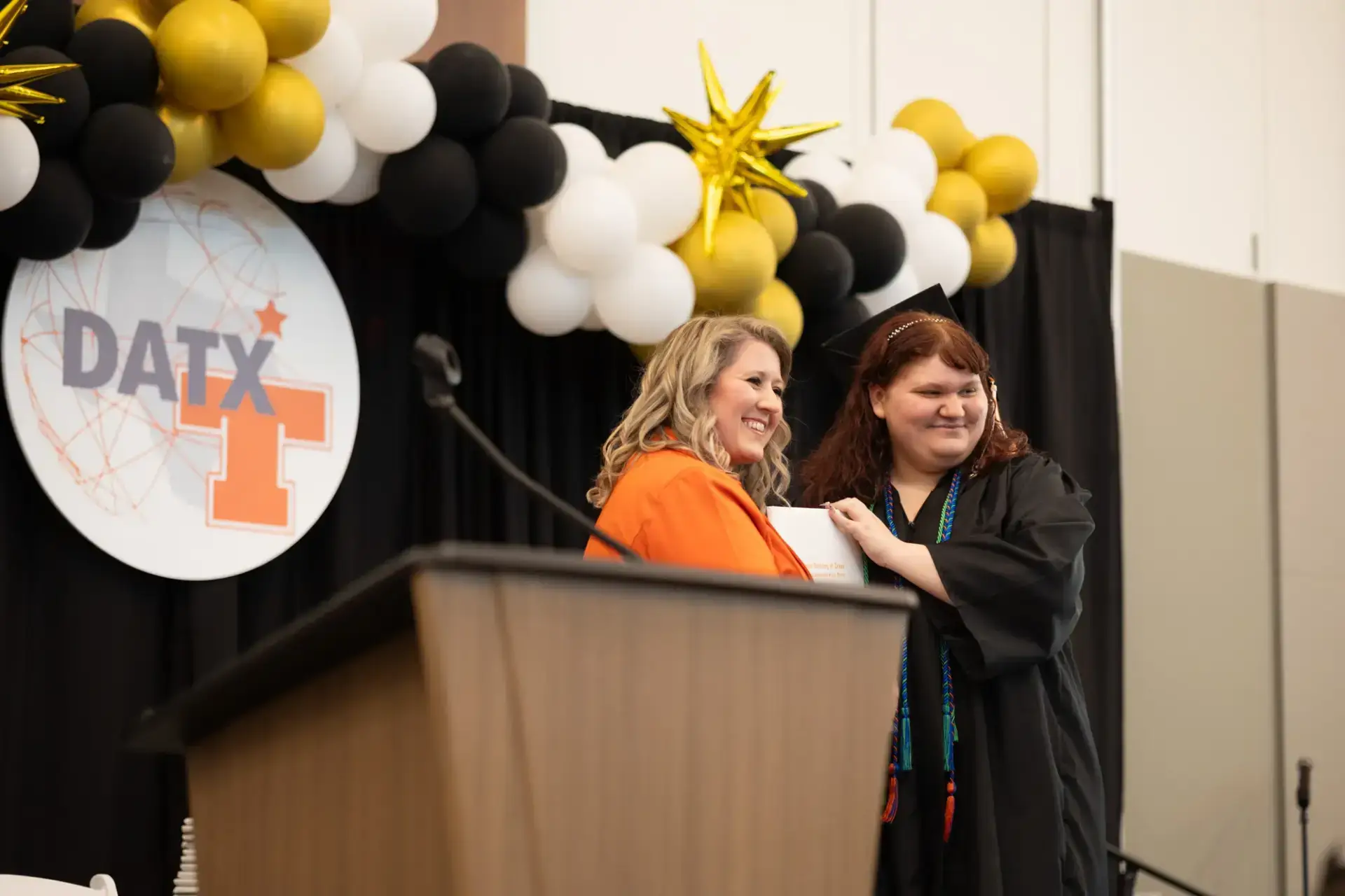 Two women smiling during a graduation ceremony.