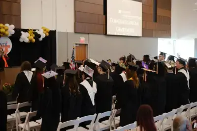 Graduates in caps and gowns face forward at a ceremony.